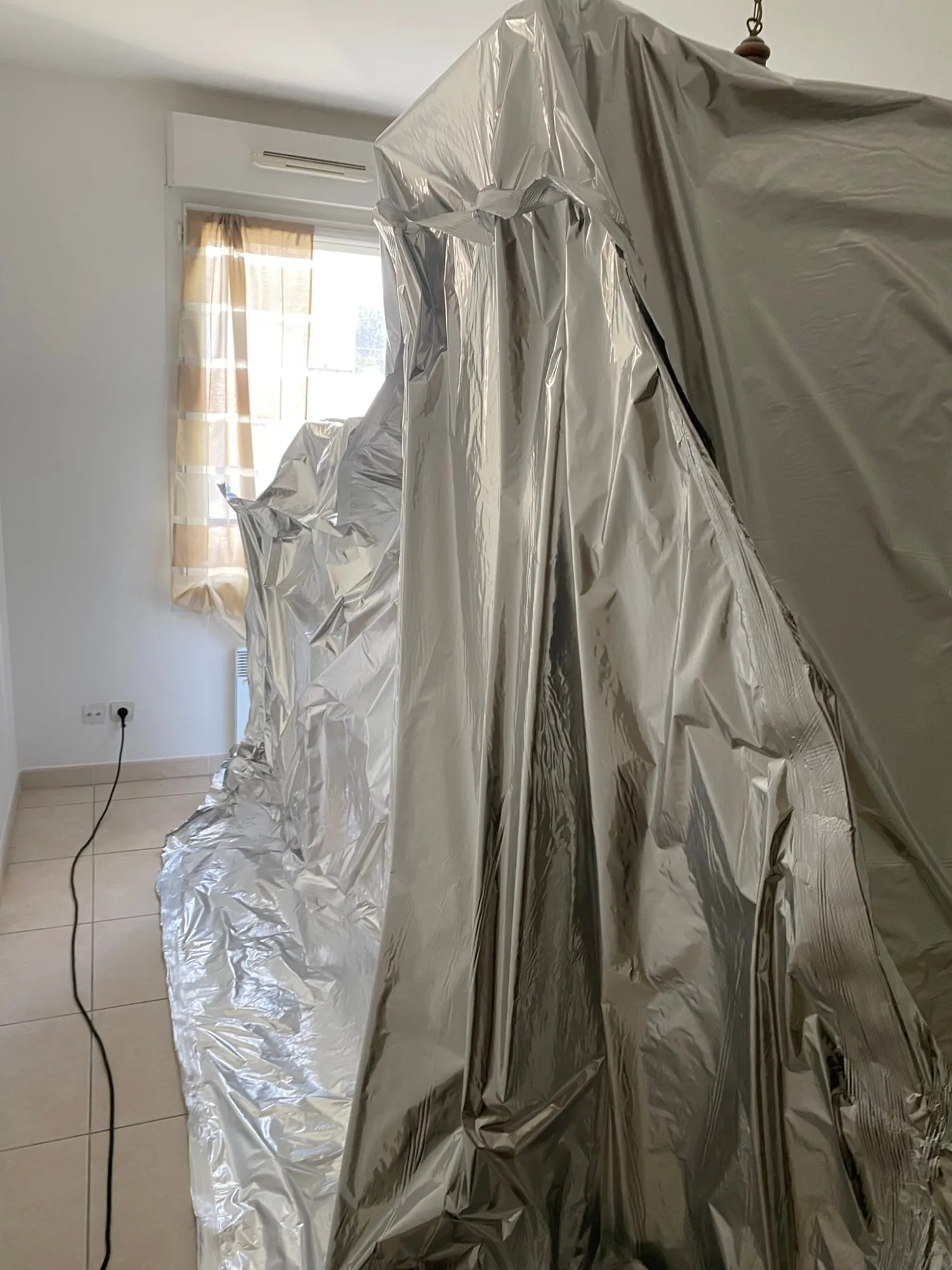 Enveloppe étanche en film barrière aluminium fermée autour d’un ensemble de meubles, dans une chambre