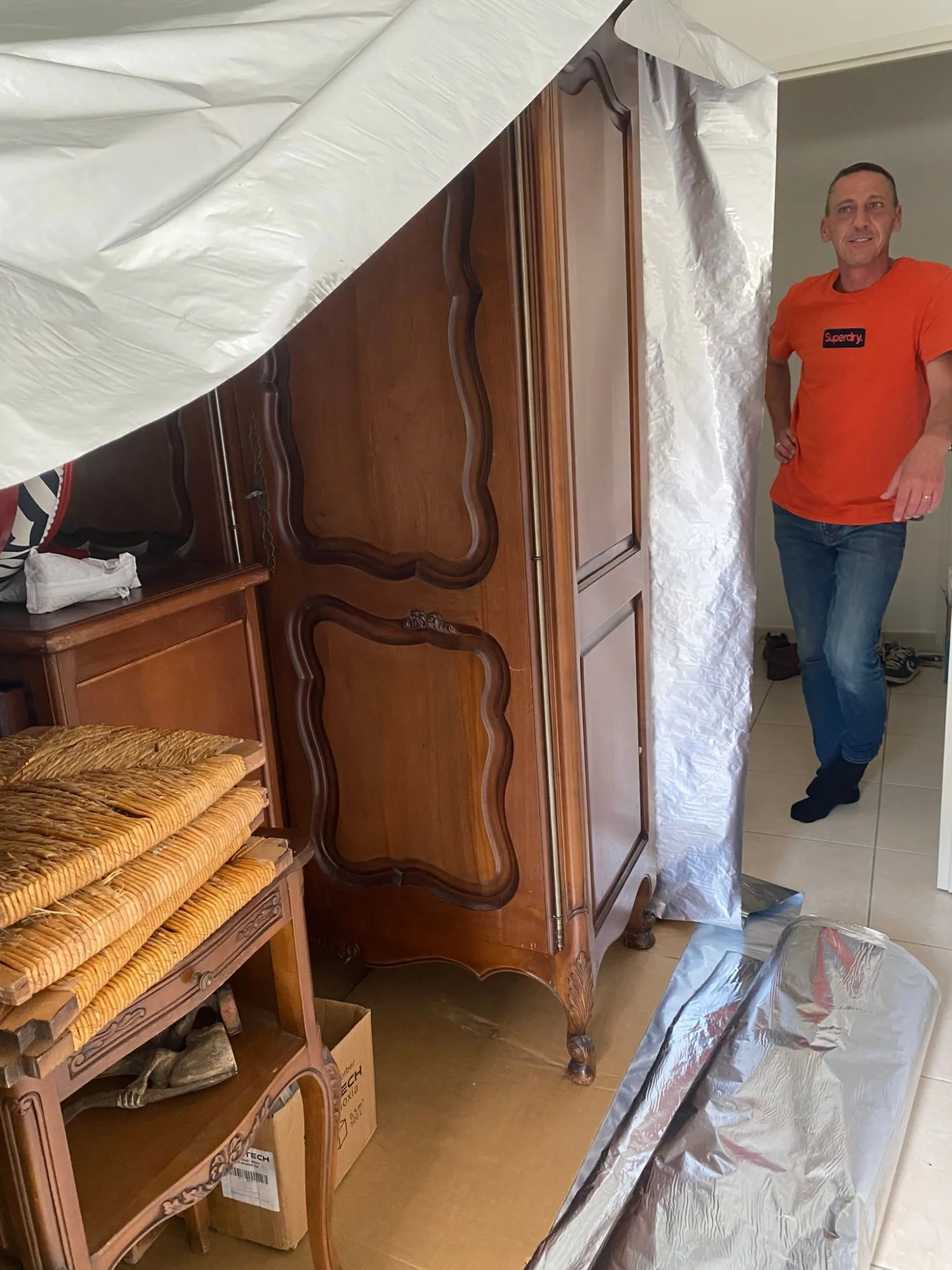 Installation d’une enveloppe d’anoxie autour d’une armoire ancienne et de chaises paillées dans une chambre