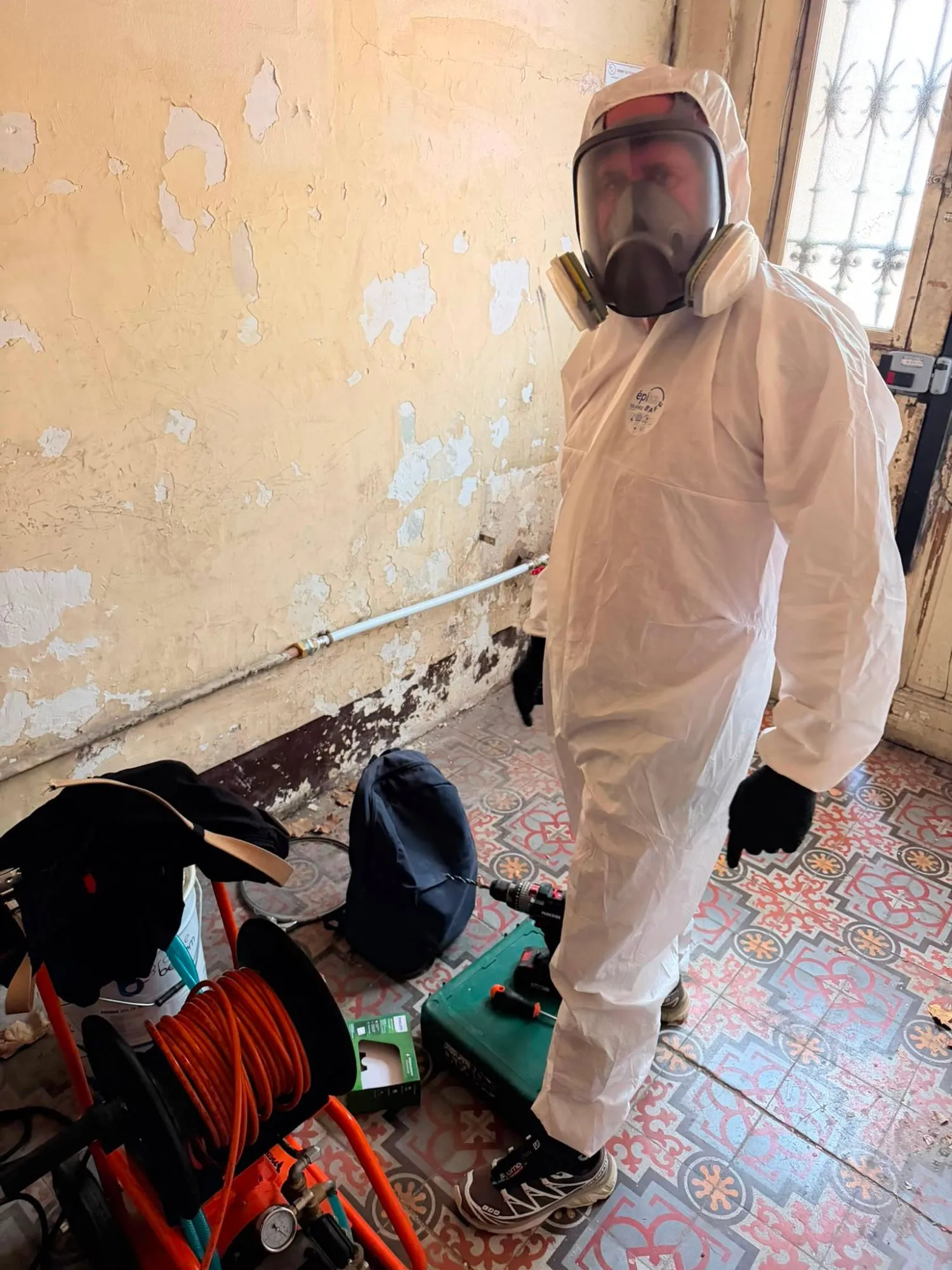 Technicien en combinaison et masque intégral à cartouches, avec le matériel de traitement, dans le hall d’un immeuble ancien à Marseille