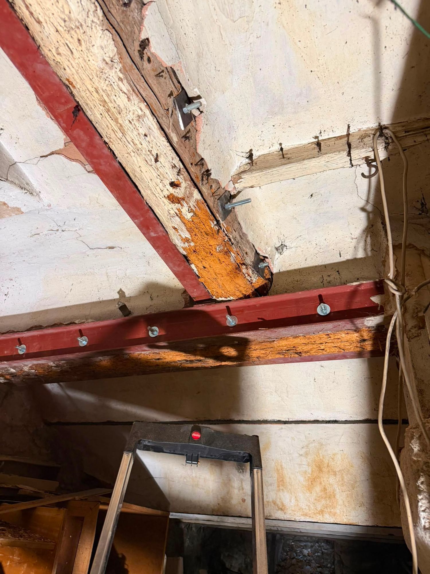 Poutres anciennes attaquées par la vrillette, bûchées jusqu'au bois clair, doublées de profilés métalliques rouges boulonnés, dans un bâtiment ancien