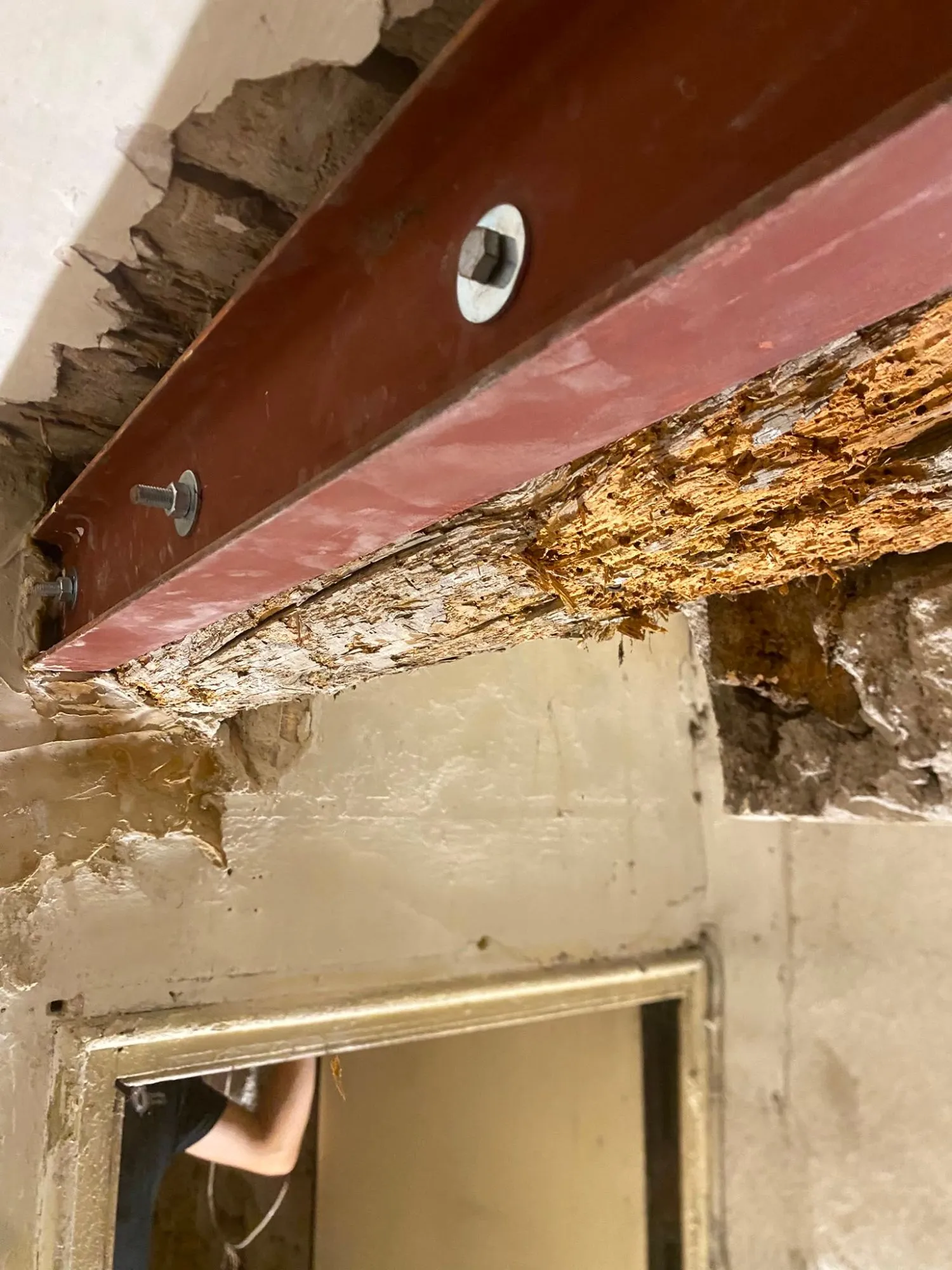 Poutre ancienne au bois abîmé, doublée d’un profilé métallique fixé par des boulons, au-dessus d’une porte