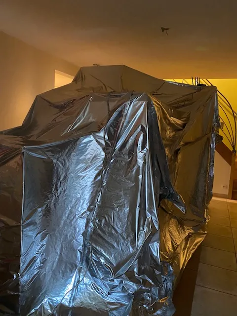 Grande enveloppe étanche en film aluminium au milieu d’une pièce, près d’un escalier à rampe métallique