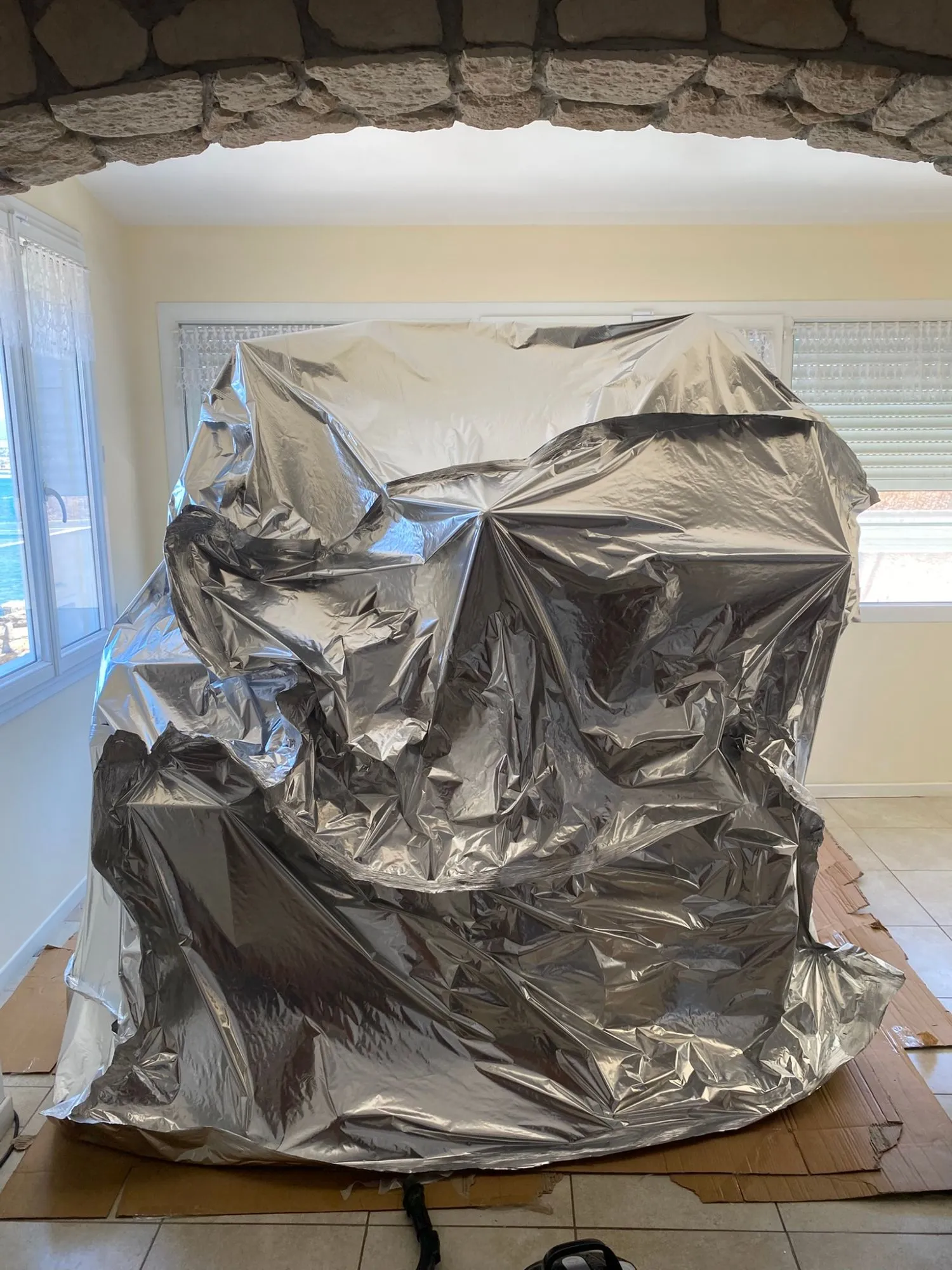 Grande enveloppe étanche en film aluminium fermée sur des cartons, vue à travers une arche en pierre