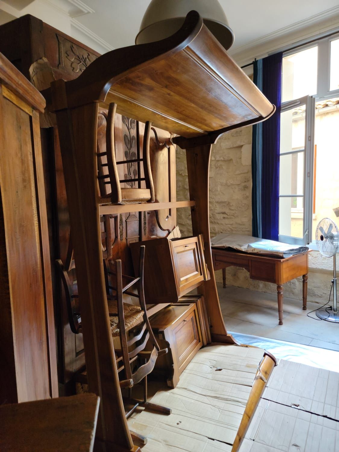 Meubles anciens regroupés sur des cartons avant l'anoxie : grande pièce à fronton courbé, armoire sculptée, chaises paillées et éléments à abattant